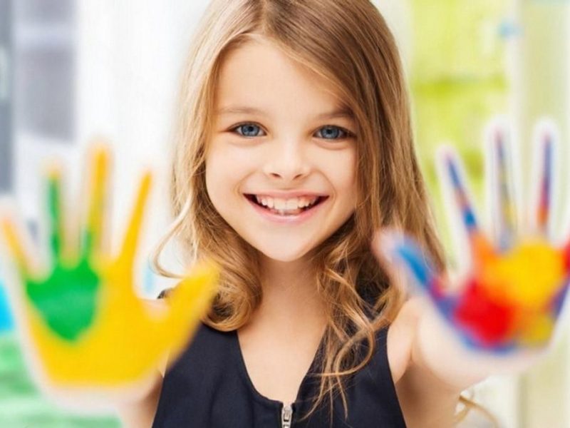 Smiling girl in the UAE showing hands covered in bright finger paints
