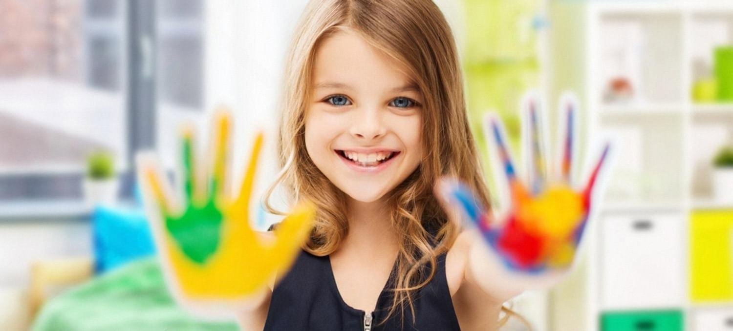 Smiling girl in the UAE showing hands covered in bright finger paints