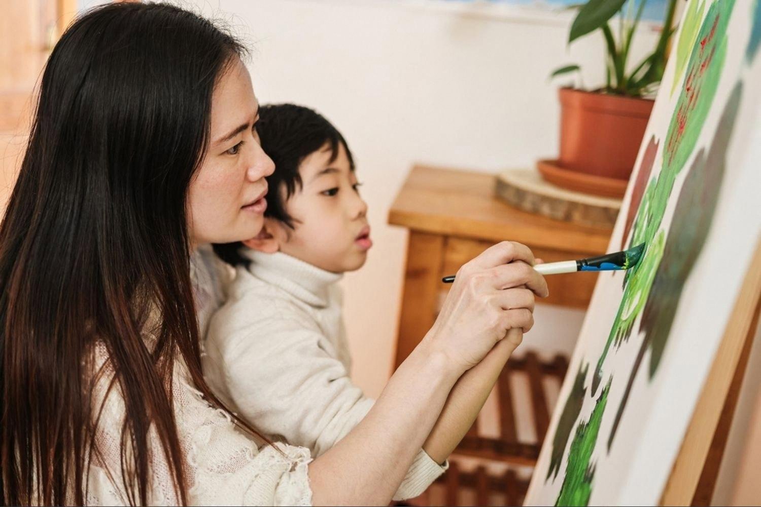 Mother helping her child paint on a large easel canvas at home